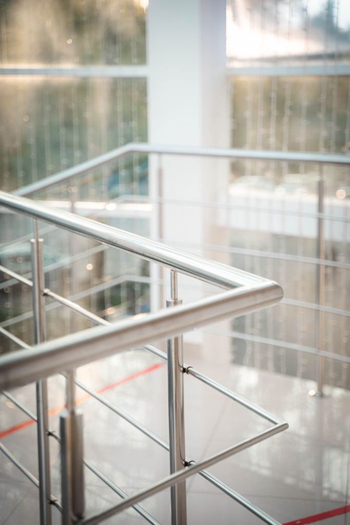 A close-up view of a stainless steel staircase railing in a sunlit indoor setting, highlighting modern design.
